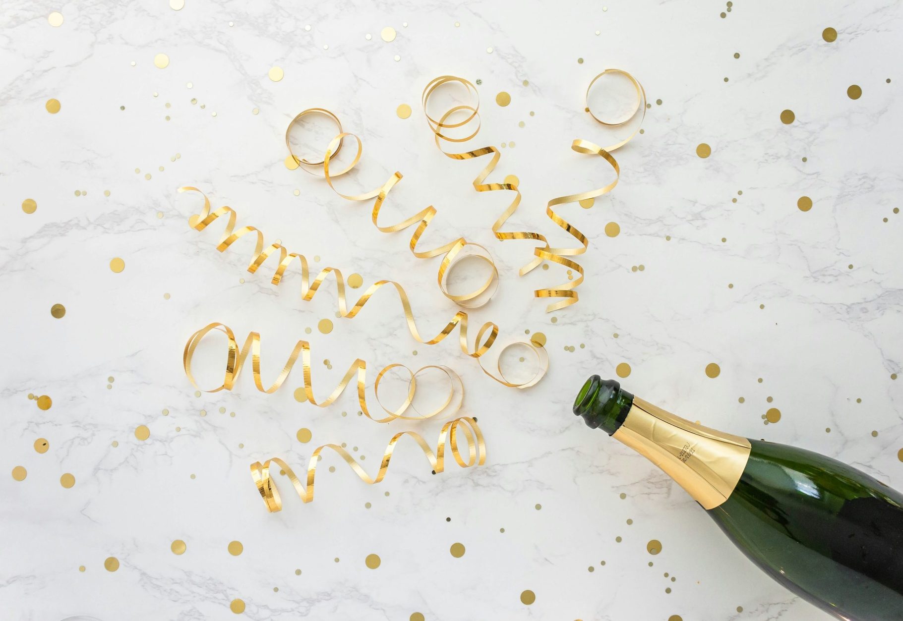 Congratulation_Quelle_Maryam Sicard_Unsplash Offene_sektflasche_liegend_mit_goldenen_Luftschlangen_und_konfetti
